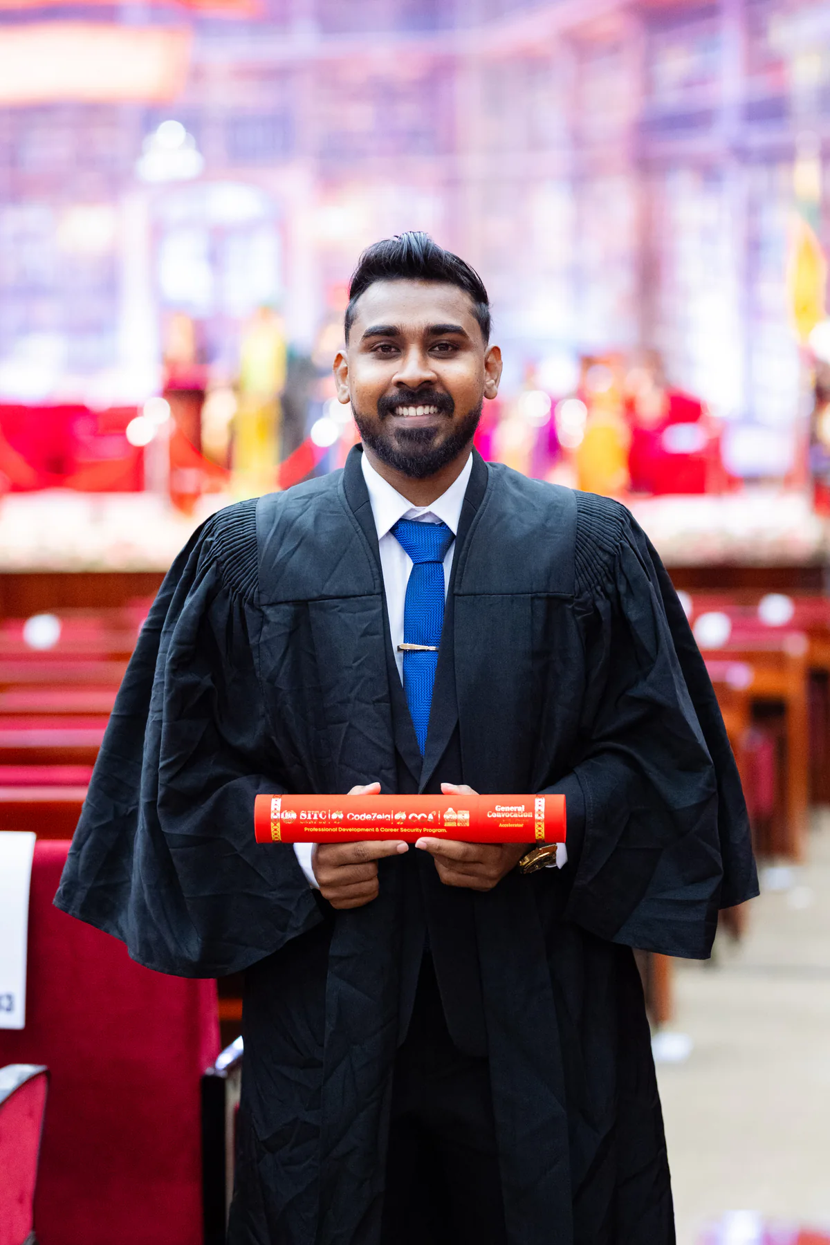 A CCA graduate holding his convocation scroll inside the auditorium