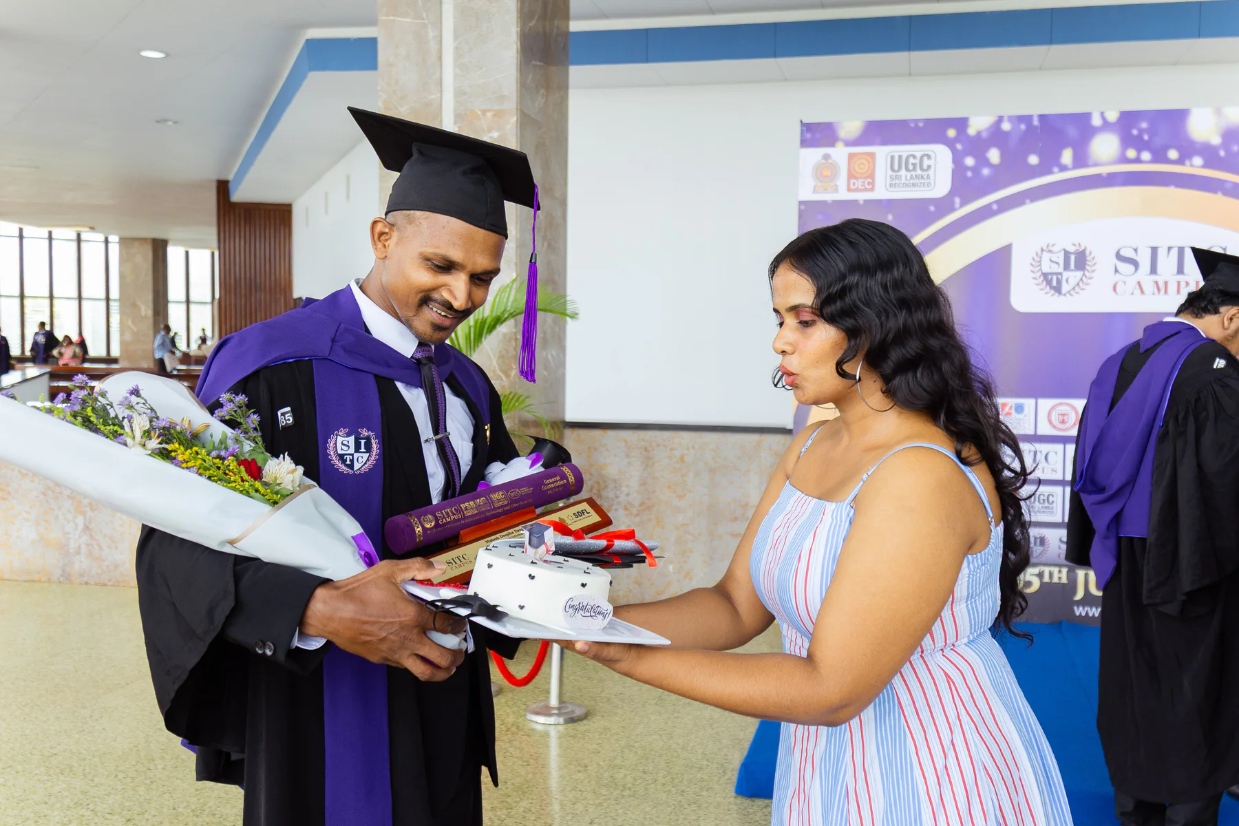 A graduate receiving flowers, a keepsake and a celebration cake