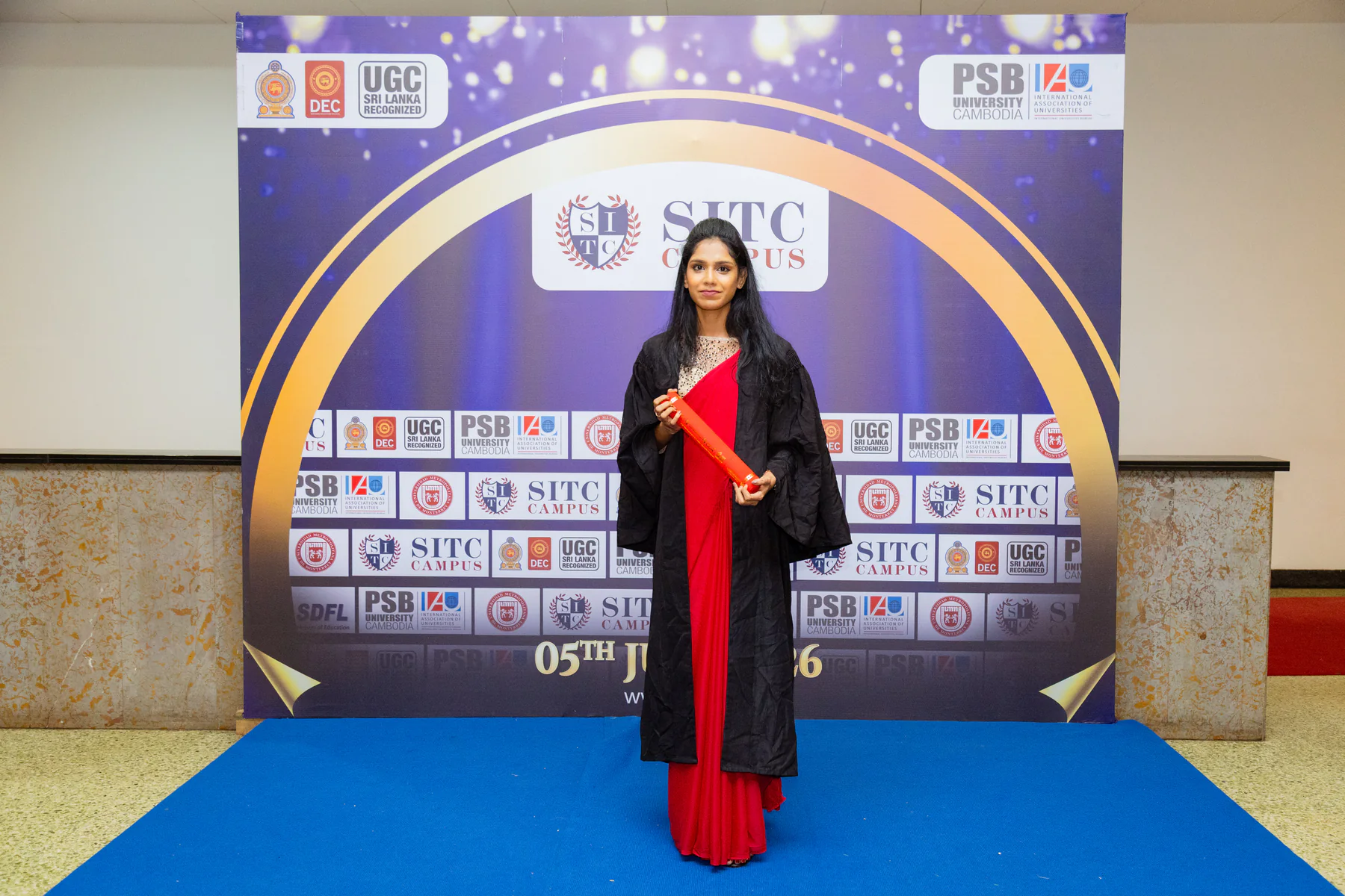 A graduate standing with her scroll at the convocation portrait wall