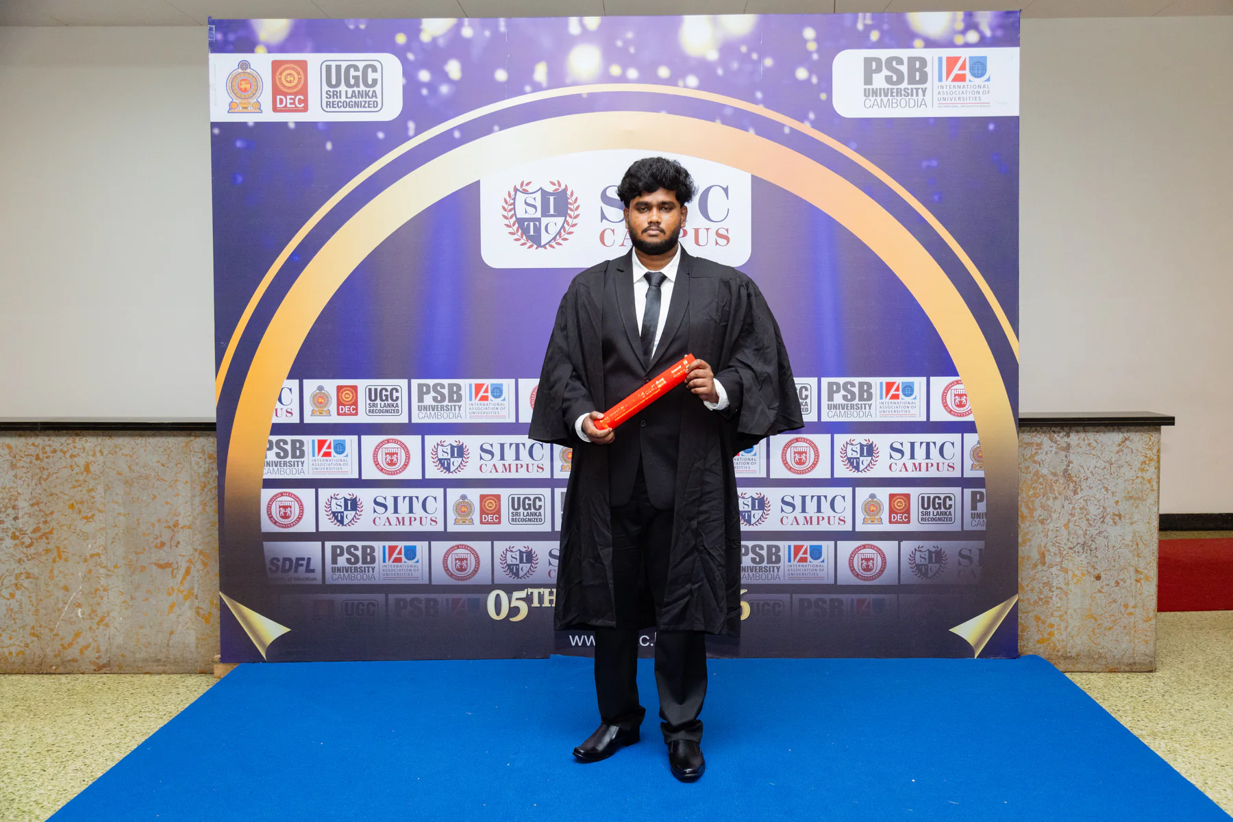 A graduate holding a scroll at the convocation portrait wall