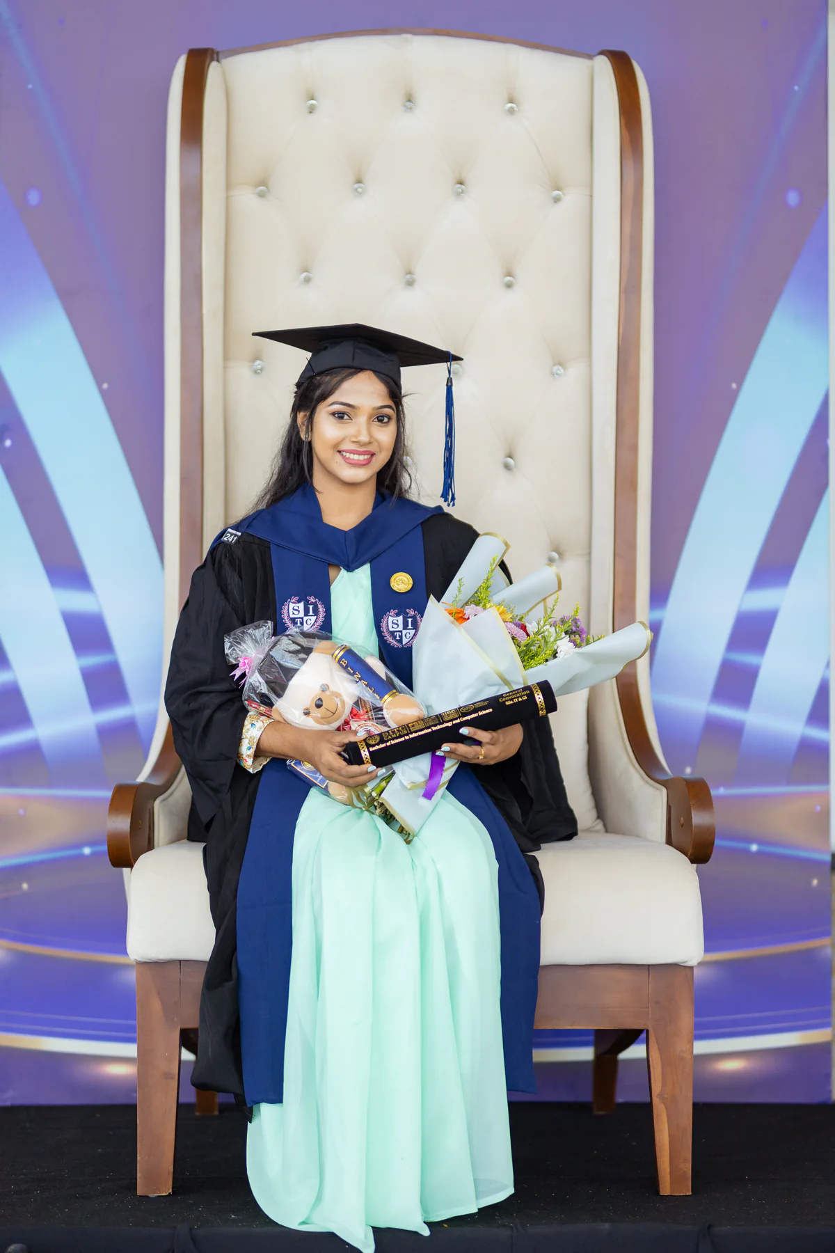 A graduate in academic dress holding flowers and her graduation scroll