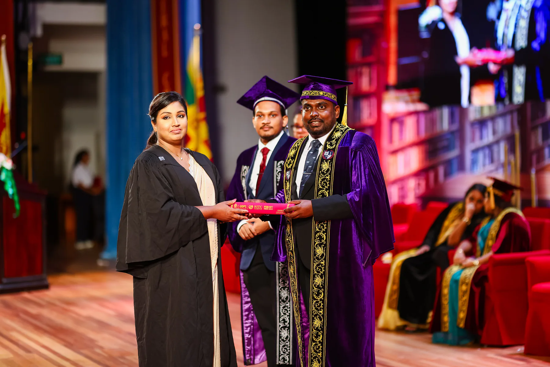 A graduate receiving recognition with academic representatives on stage